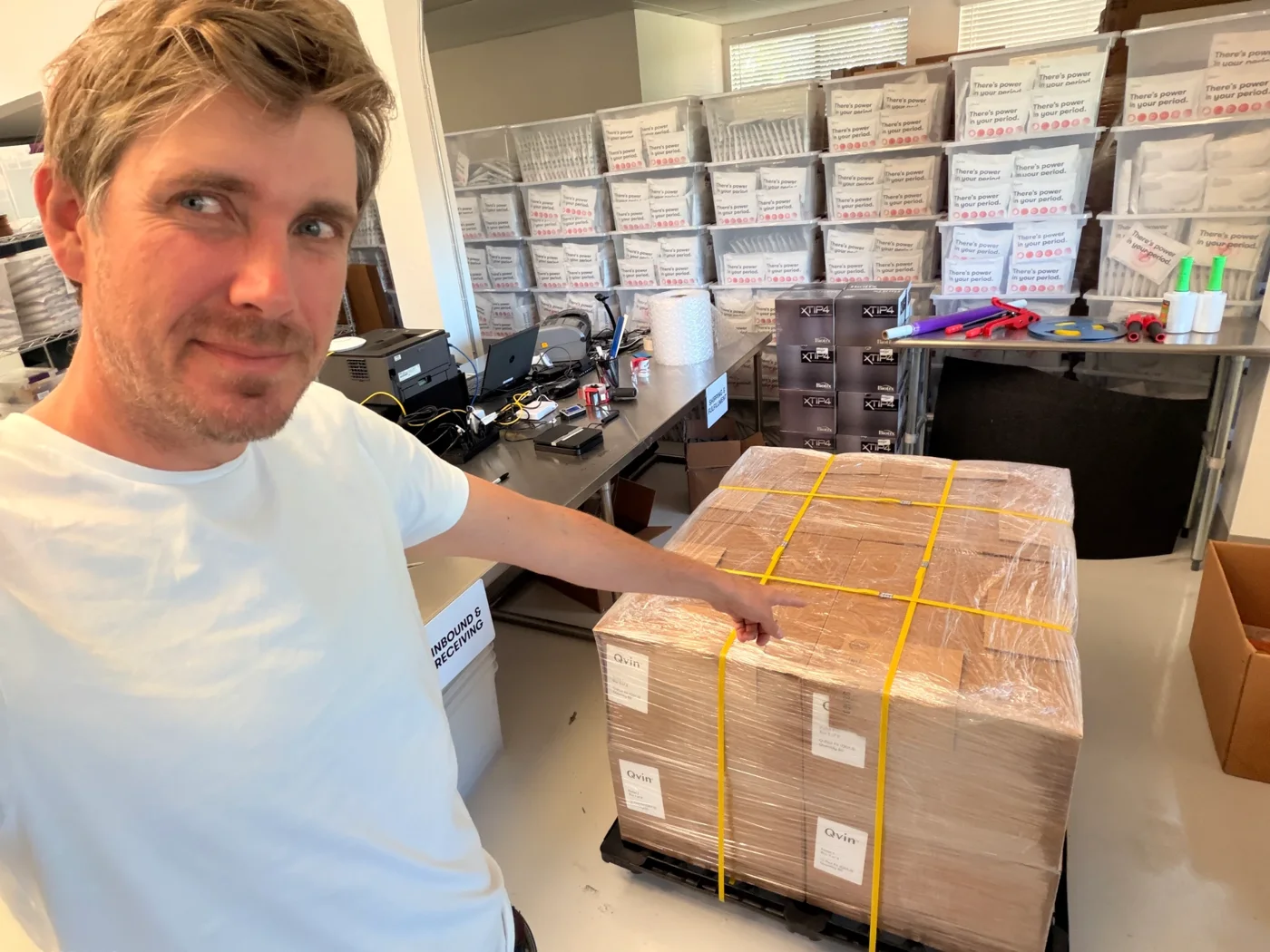 A Qvin team member pointing at a wrapped pallet of Q-Pad Kit cases